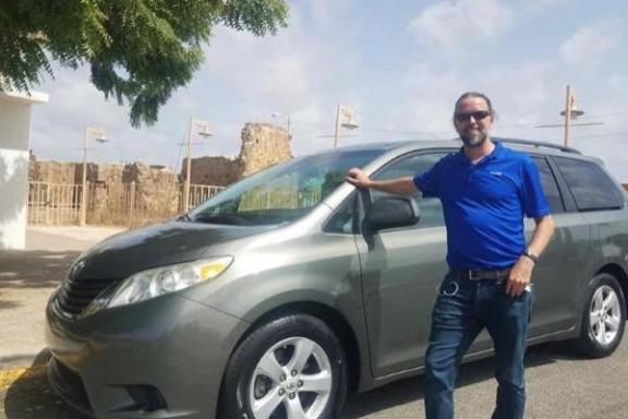 a man standing in front of a blue car parked in a parking lot